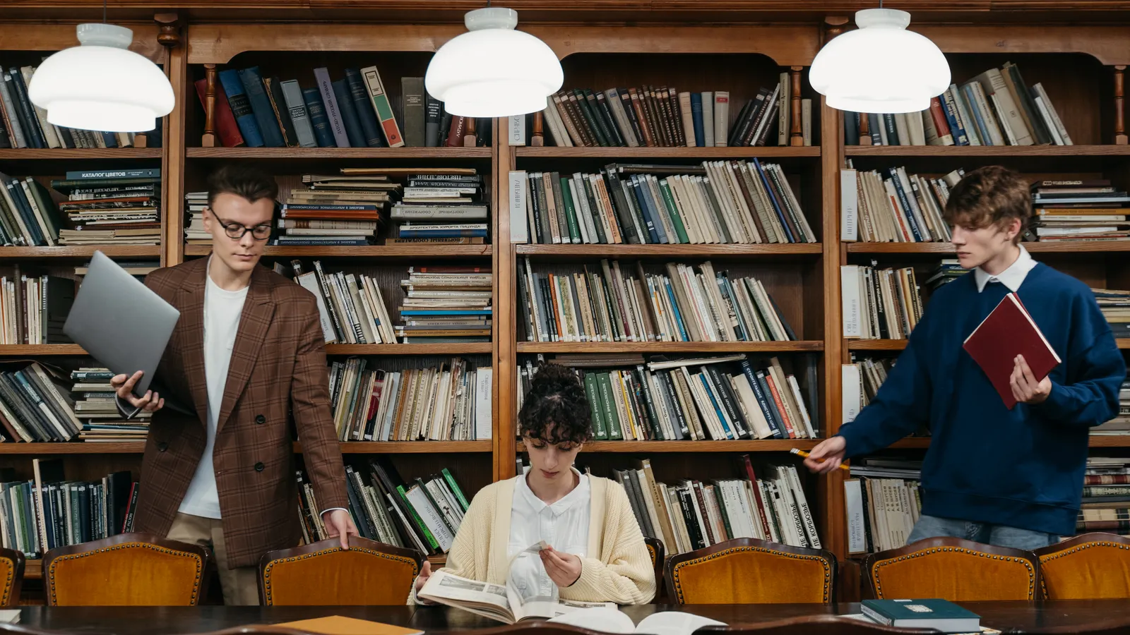 Students studying at tables surrounded by library bookshelves