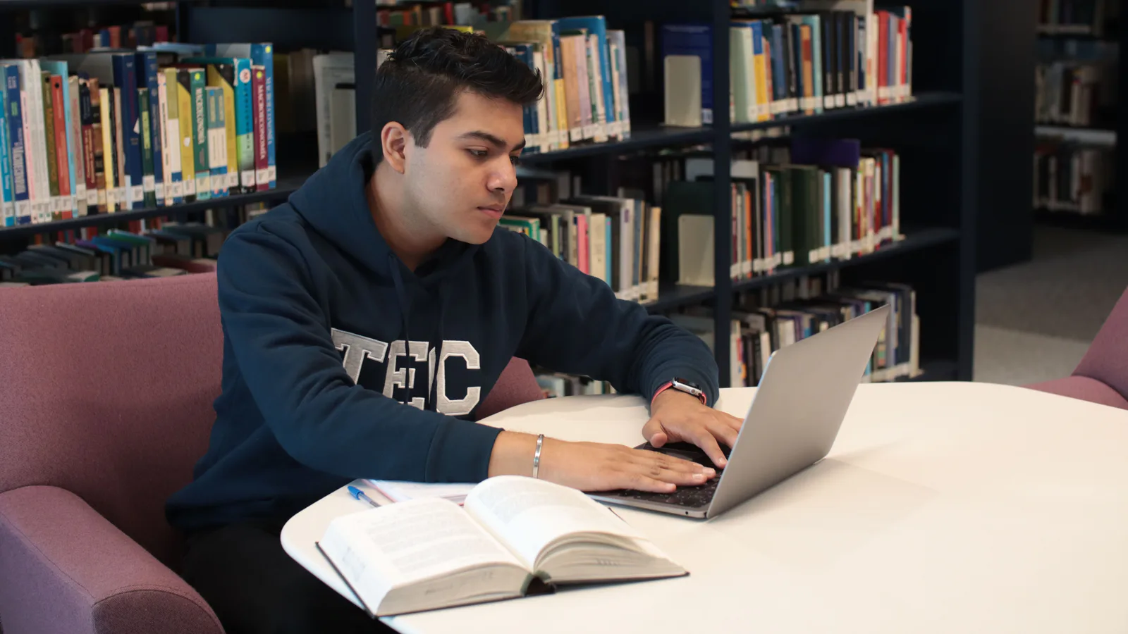 Student researching with a laptop and open books in a library