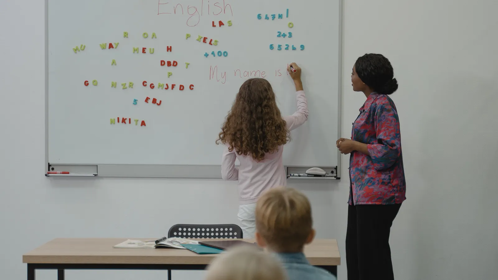 A teacher guiding students through letters on a classroom whiteboard