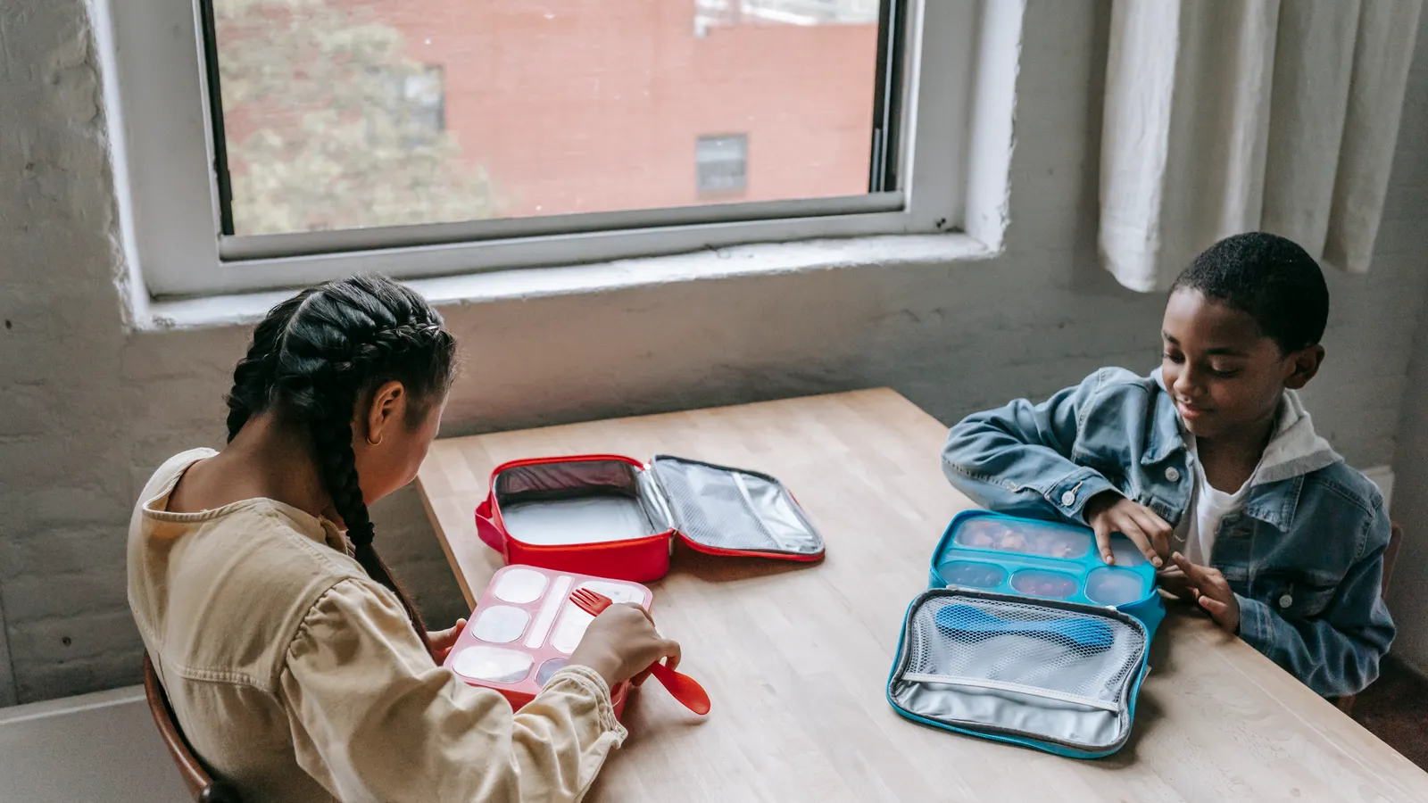 Children with lunch boxes seated together beside a classroom window