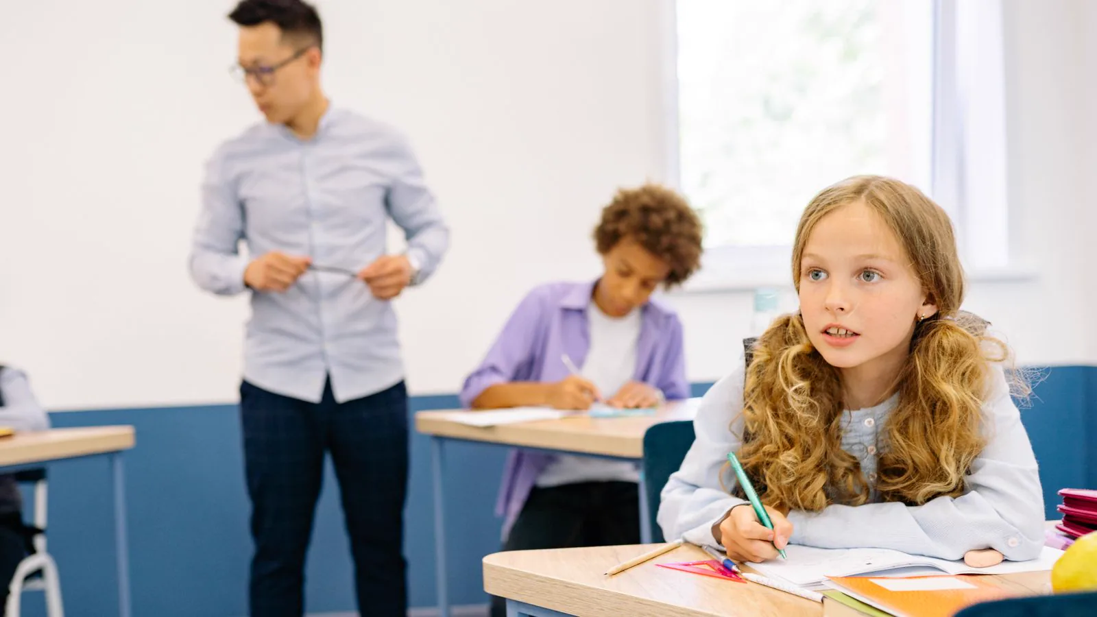 Students working in a classroom while a teacher stands nearby